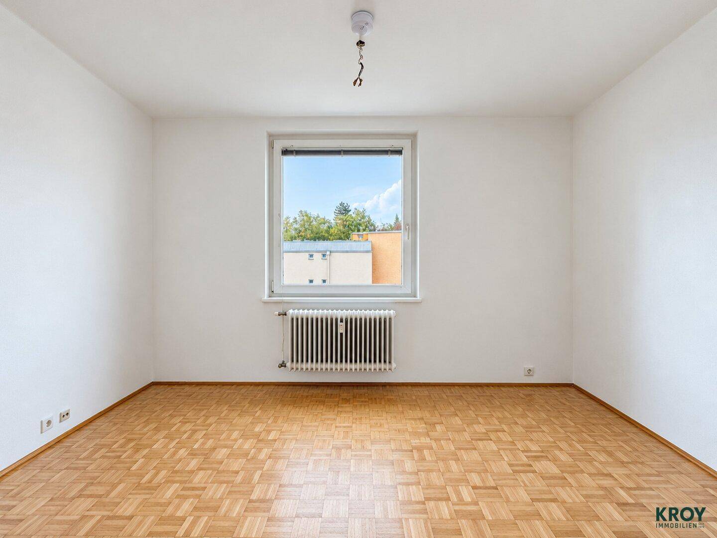 Lichtdurchflutetes Zimmer mit Parkettboden und Heizkörper unter dem Fenster.