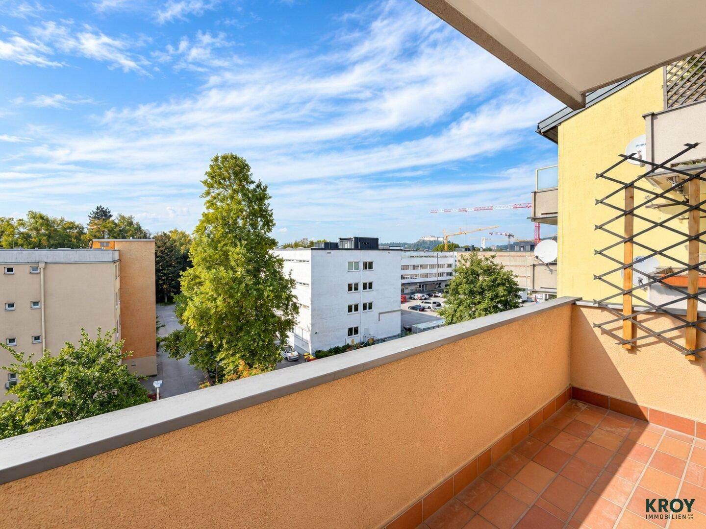 Balkon mit Terrakotta-Fliesen und Blick auf die umliegenden Gebäude und Bäume.