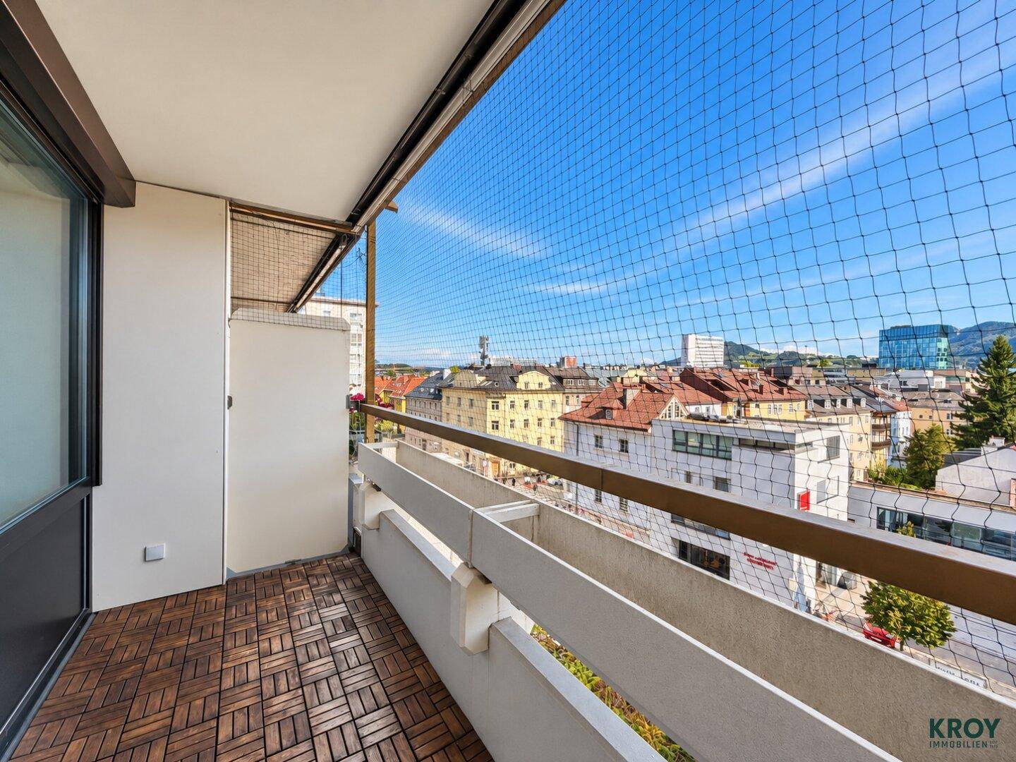 Geräumiger Balkon mit Holzboden und Schutznetz, mit Panoramablick über die Stadt und die Landschaft.