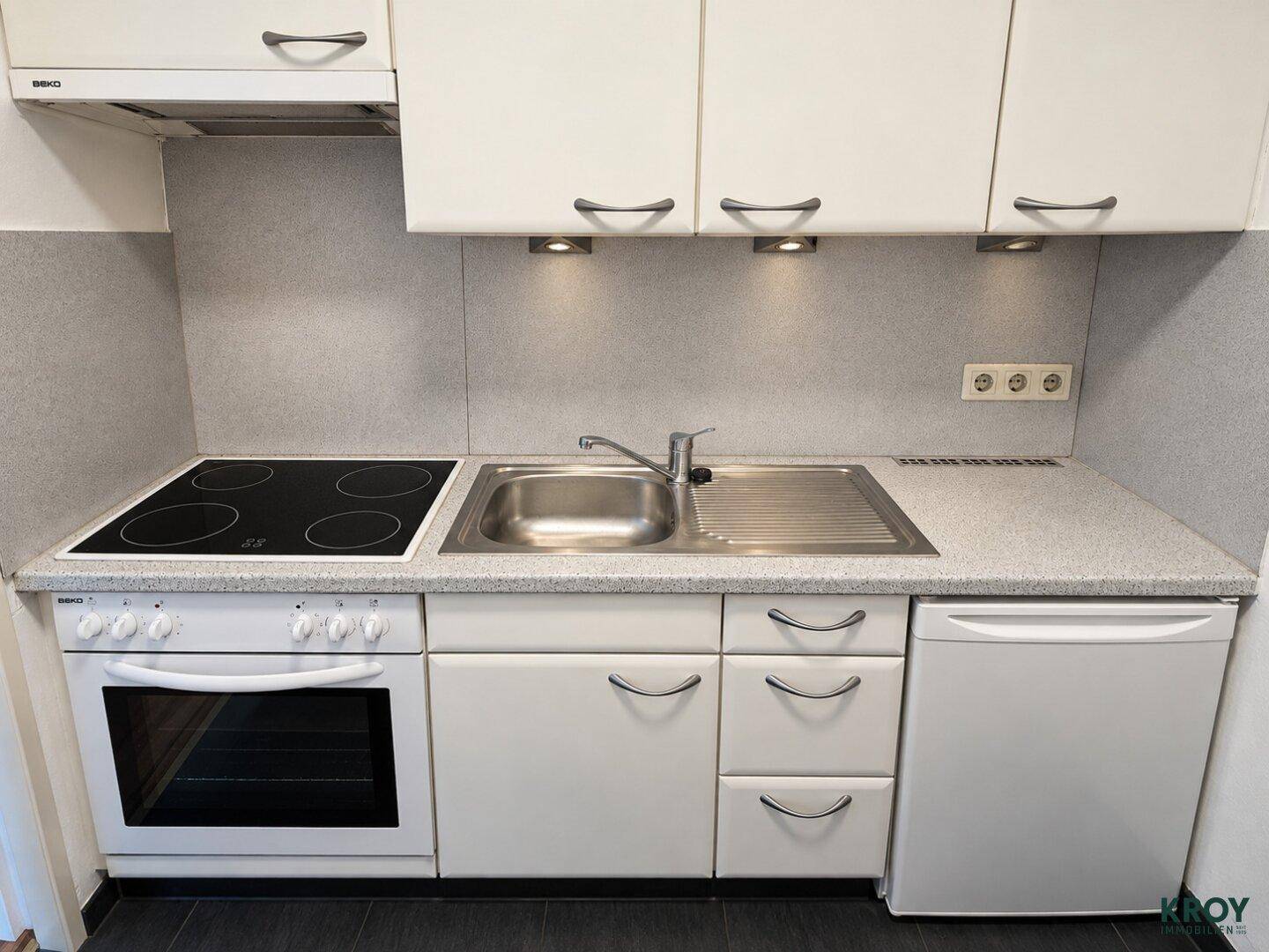 Kompakte Küchenzeile mit Herd, Spüle und Kühlschrank, ideal für kleine Wohnungen.