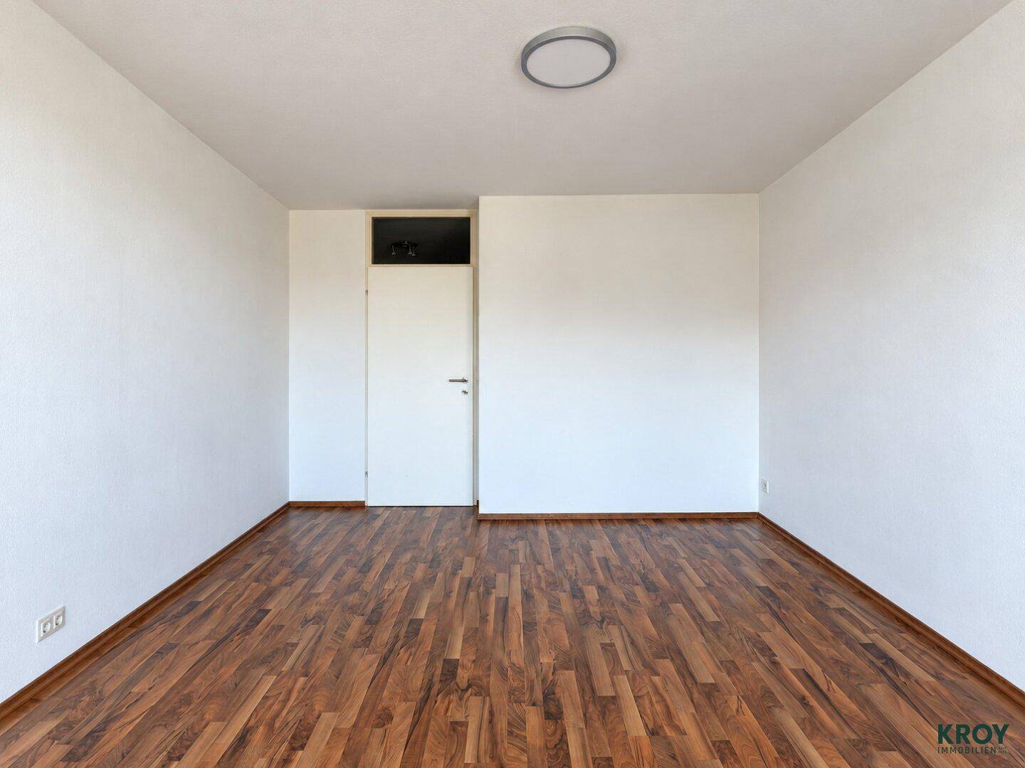 Leeres Zimmer mit Holzboden und weiß gestrichenen Wänden, bereit zur individuellen Gestaltung.