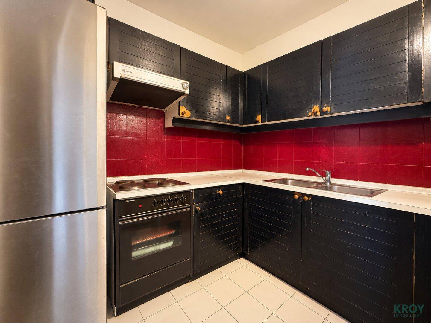 Funktionale Küche mit schwarzen Holzschränken, roten Fliesen, Herd und Edelstahlkühlschrank.