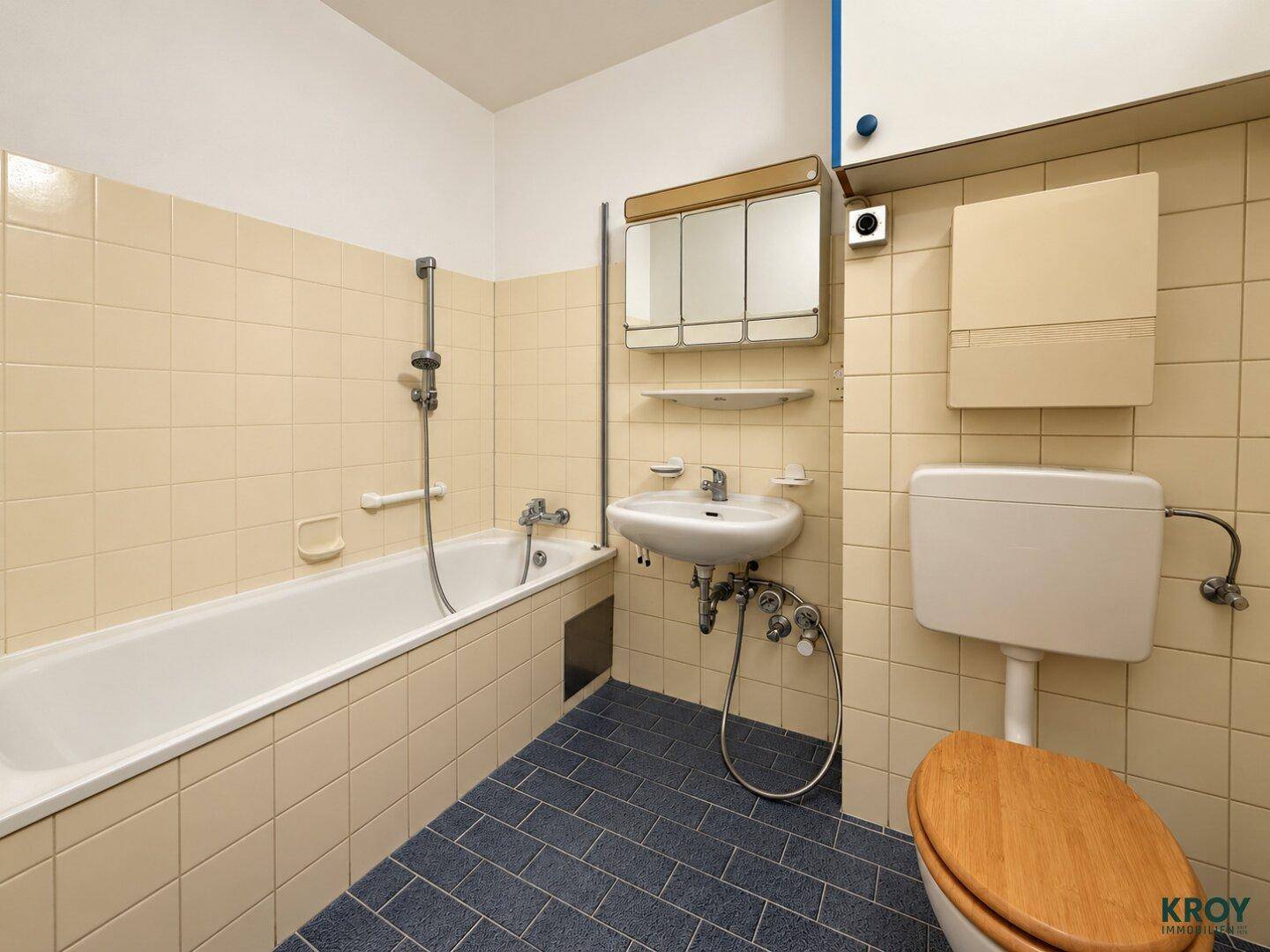 Badezimmer mit Badewanne, WC, Einzelwaschbecken und gelben Wandfliesen im 80er-Jahre-Stil.