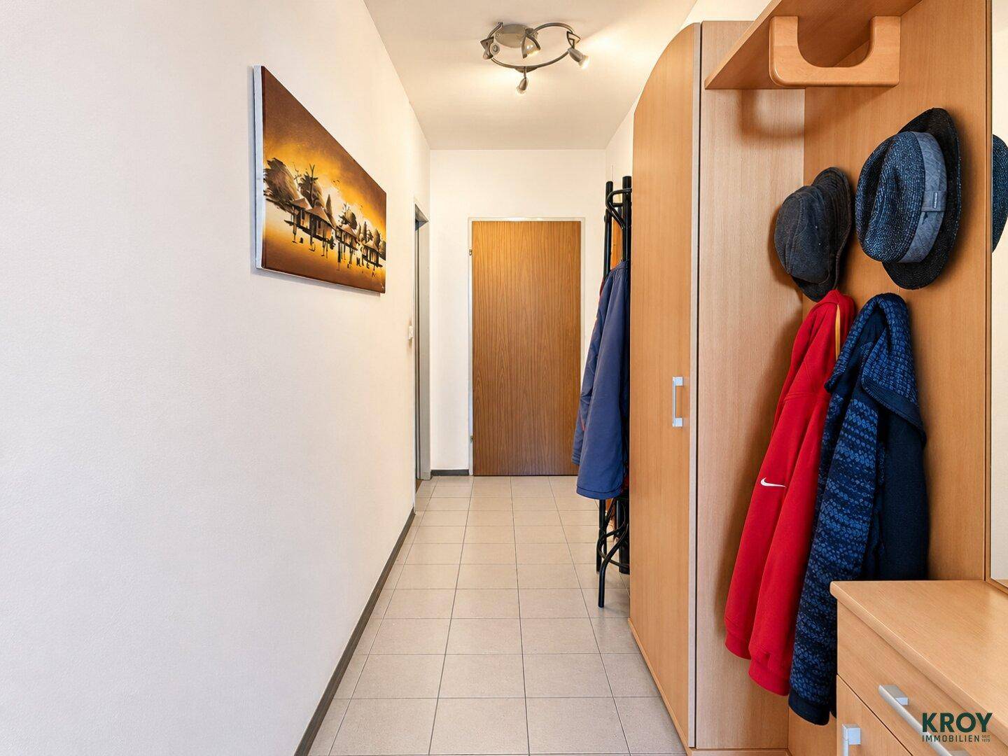Langer Flur mit heller Fliesenboden, Garderobe und schlichter Deckenleuchte.