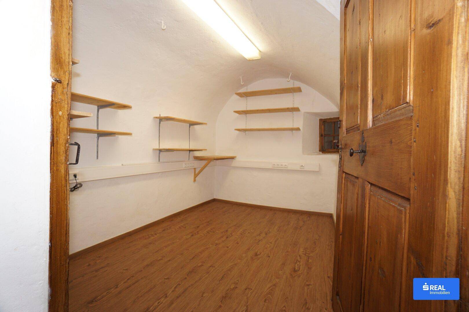 Kleiner Lagerraum mit gewölbter Decke, Holztür und praktischen Wandregalen für zusätzlichen Stauraum.