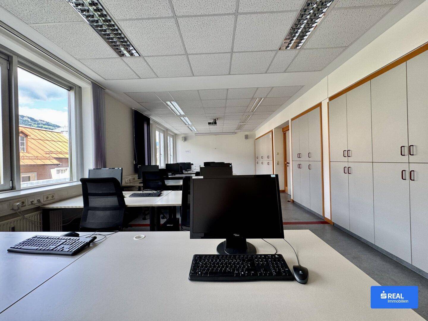 Modernes Büro mit Computern, Schreibtischen, Bürostühlen und praktischen Einbauschränken entlang der Wand.