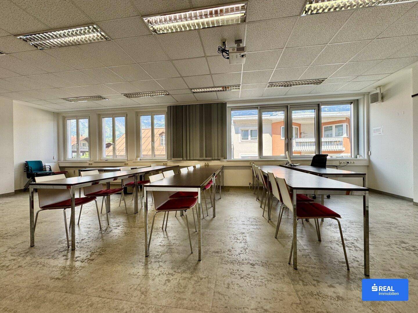 Geräumiger Konferenzraum mit vielen Tischen und Stühlen, großen Fenstern und Blick auf die Umgebung.