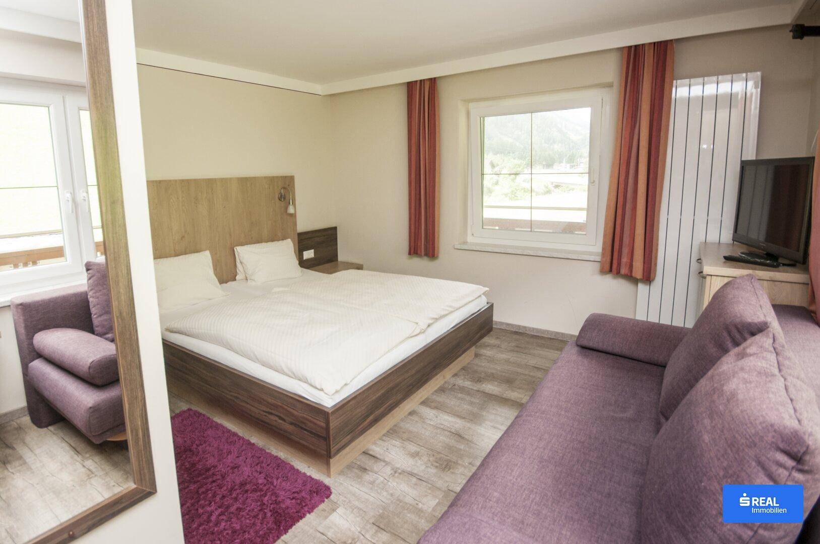 Gemütliches Schlafzimmer mit Doppelbett, zwei Sofas und Blick auf die grüne Landschaft durch das Fenster.