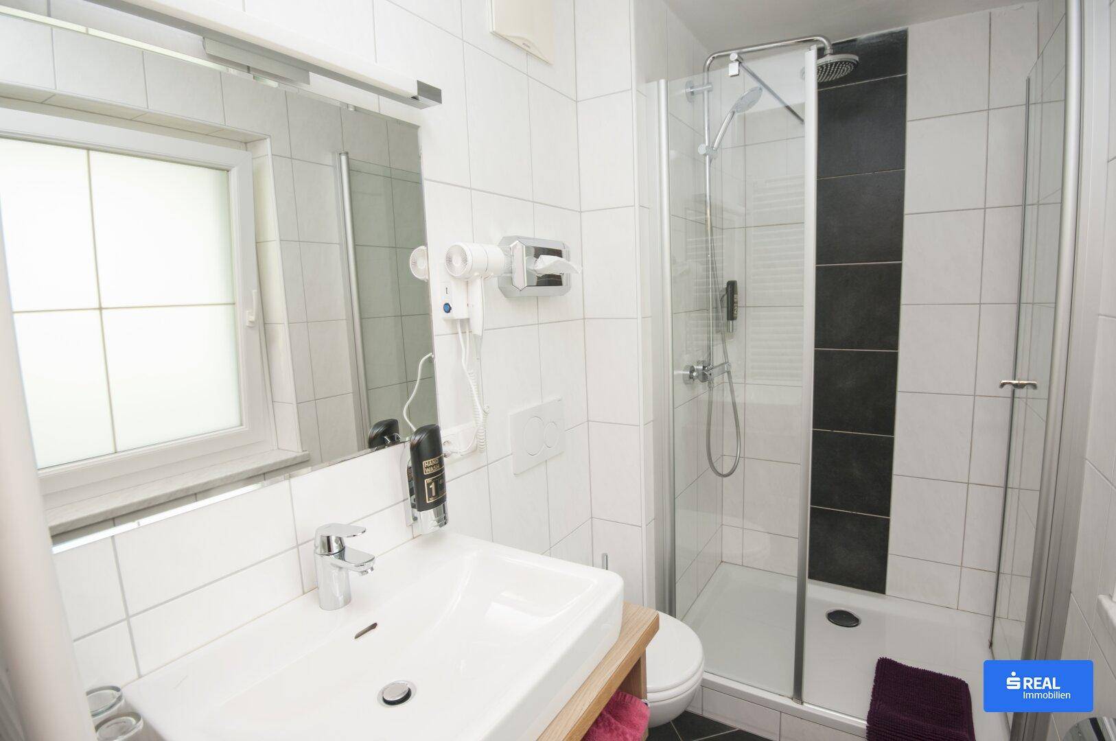 Modernes Badezimmer mit Duschkabine, Waschbecken, Spiegel und einem Fenster für Tageslicht.