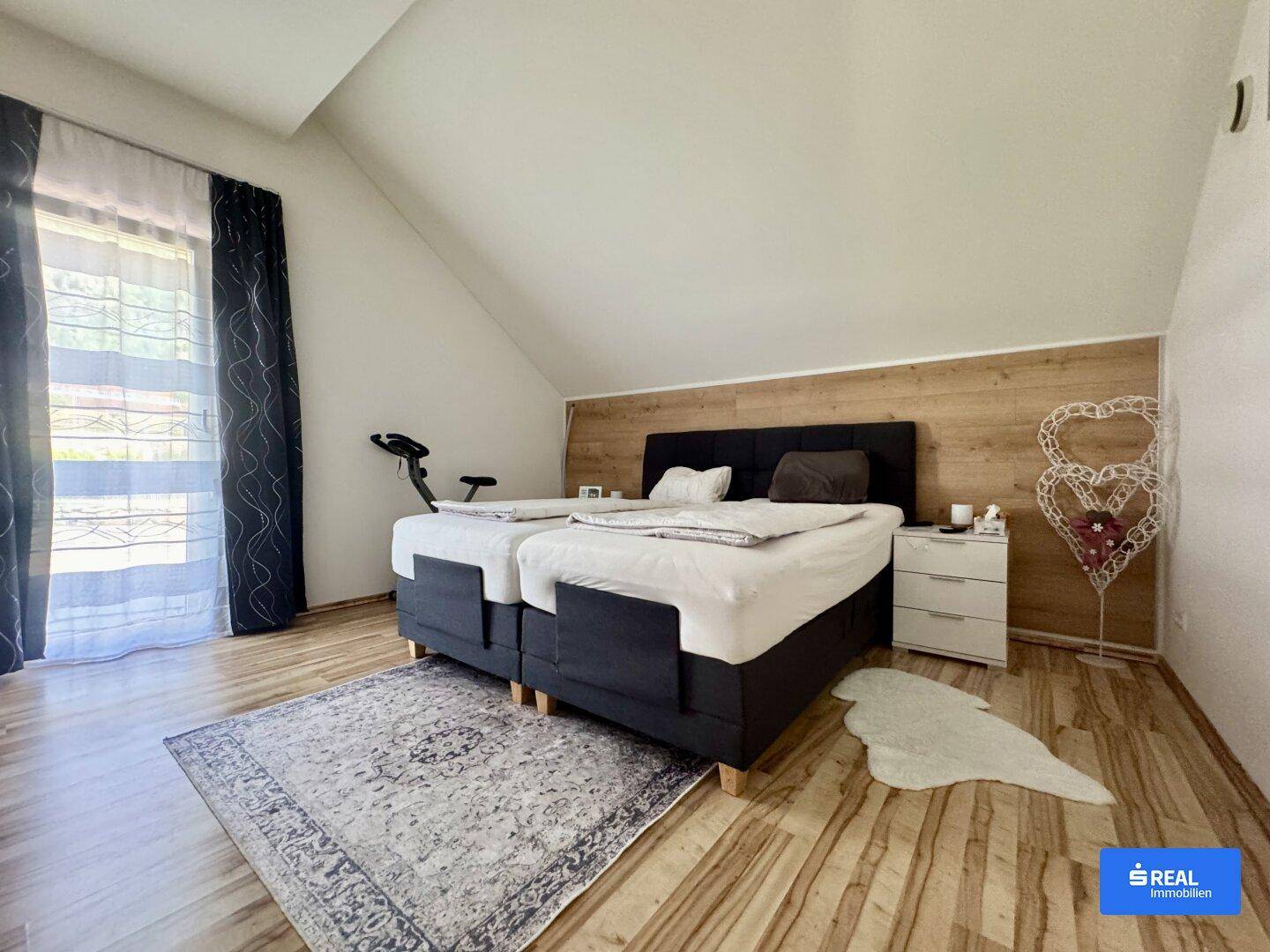 Helles Schlafzimmer im Dachgeschoss mit Doppelbett, Holzboden und schräger Decke.