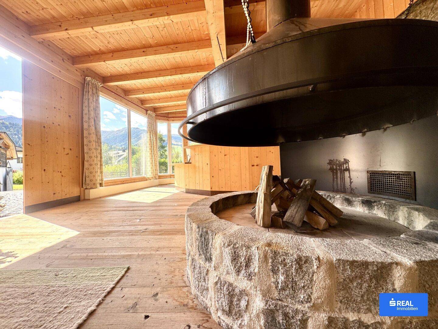 Rustikales Wohnzimmer mit Holzboden, Holzwänden und einem beeindruckenden zentralen Kamin.