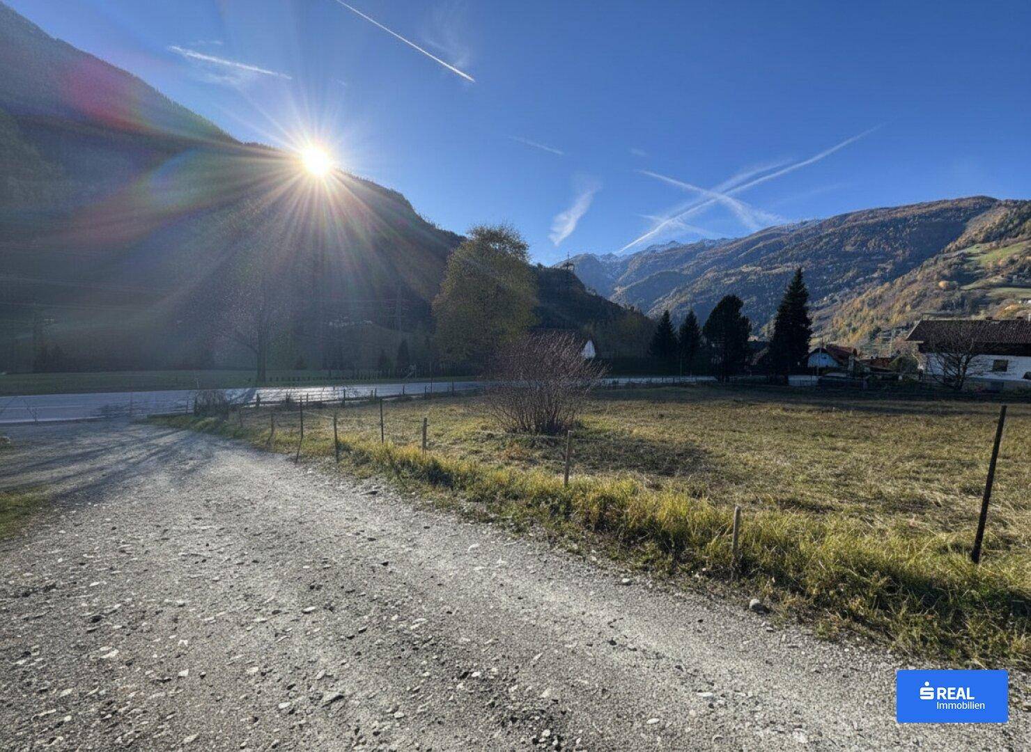 Breiter Schotterweg führt zu einem sonnigen Grundstück mit beeindruckendem Bergblick und weiten Wiesen.
