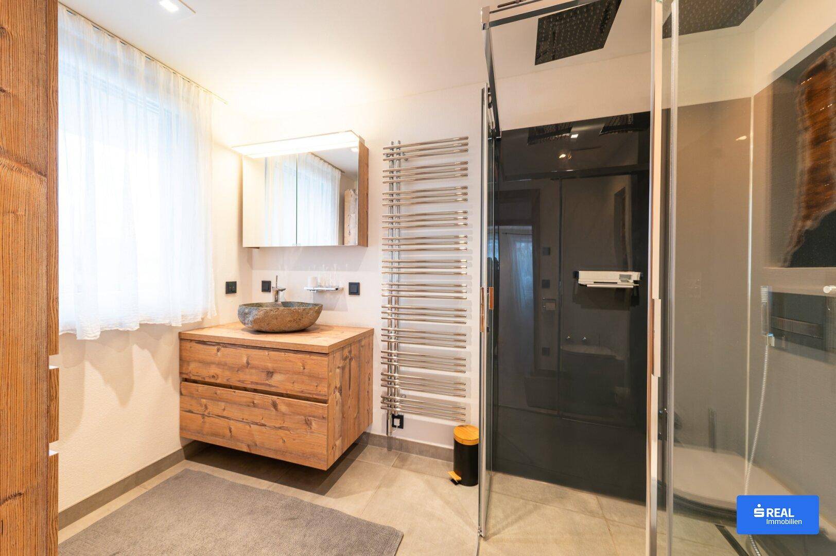 Modernes Badezimmer mit Holzwaschtisch, Steinsiphon und großer begehbarer Dusche.
