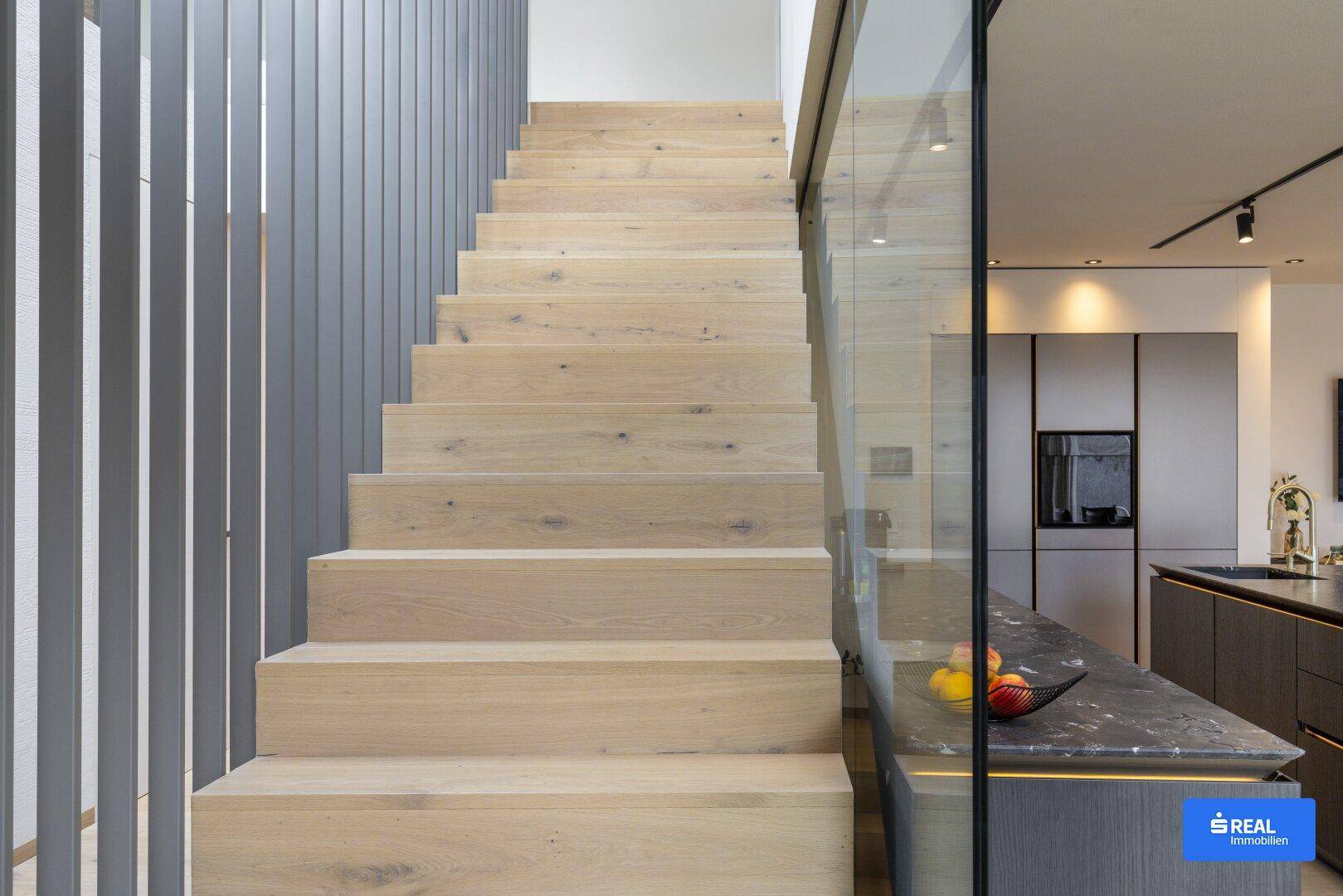 Elegante Holztreppe mit Glasgeländer, die in einem modernen Wohnraum nach oben führt.