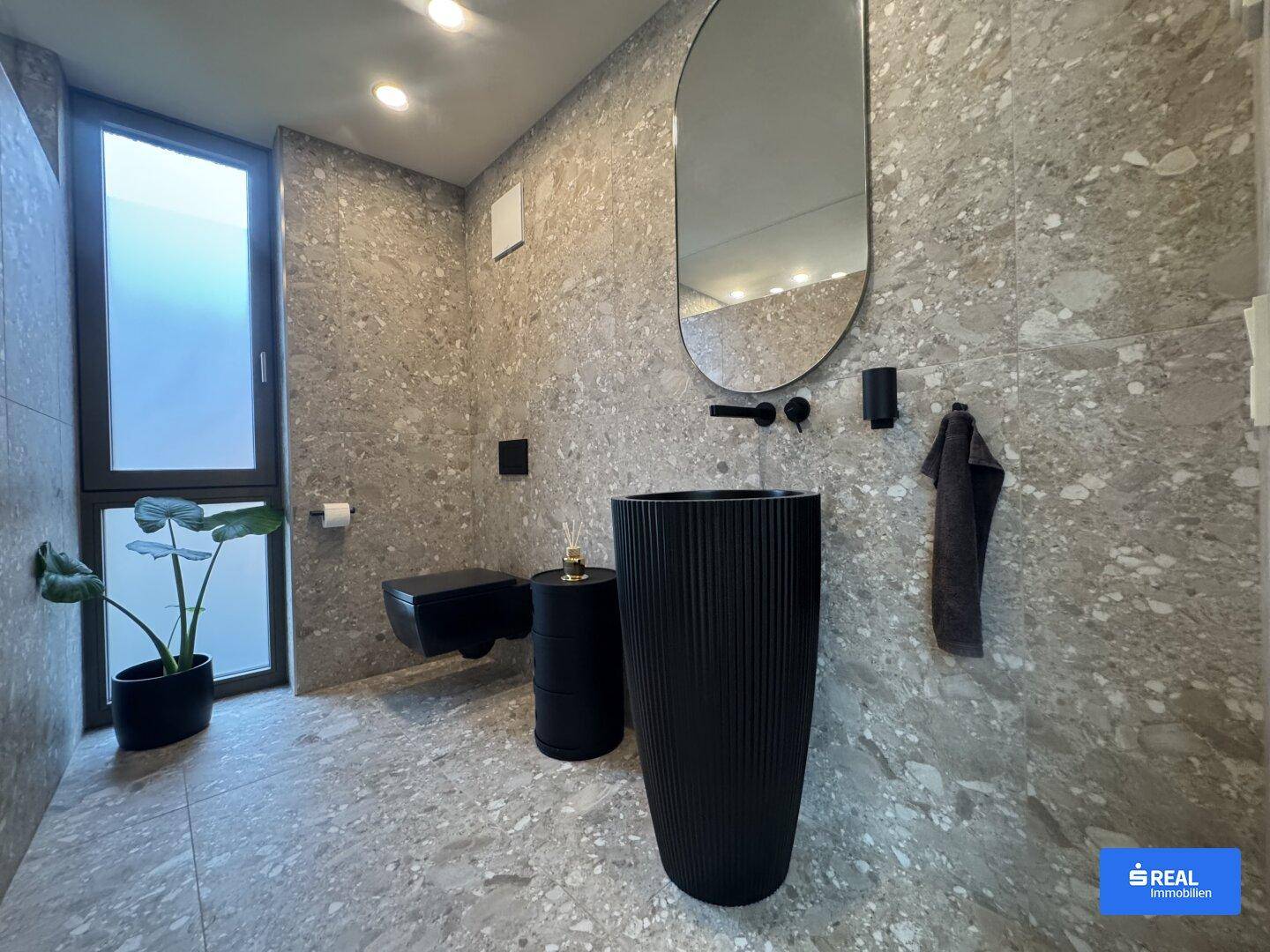Zeitgemäßes Badezimmer mit freistehendem schwarzem Waschbecken, Wand-WC und großformatigen Terrazzo-Fliesen.
