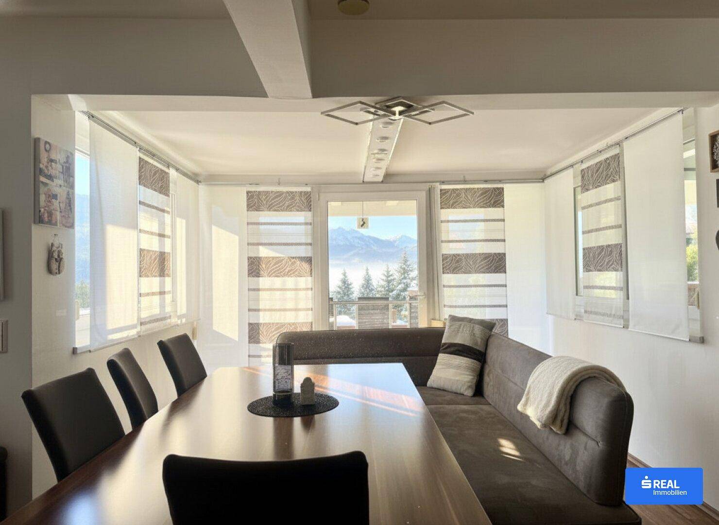 Heller Essbereich mit großem Holztisch, Sitzbank und weitem Blick auf die Berge.