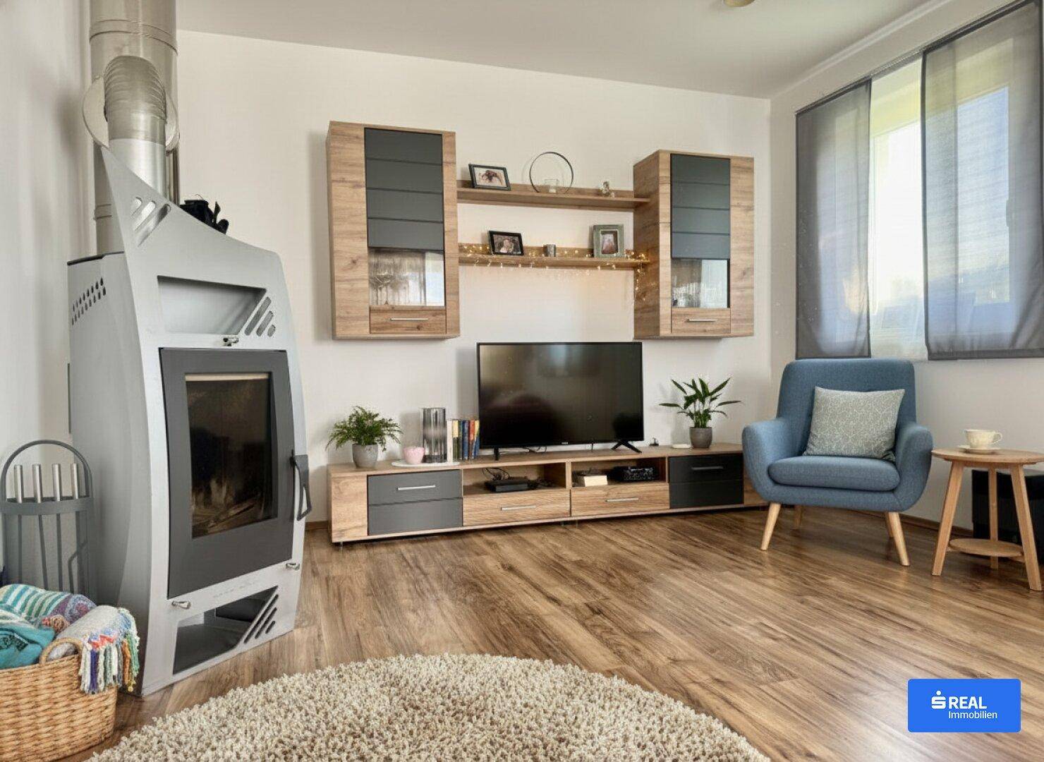 Gemütliches Wohnzimmer mit modernem Kaminofen, Holzboden und Blick ins Grüne.