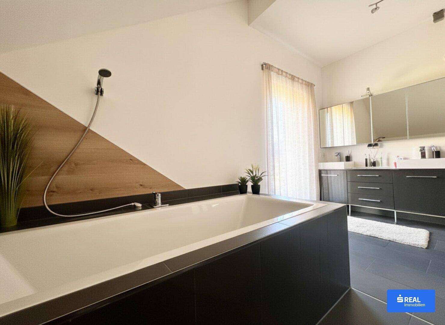 Modernes Badezimmer mit großer Badewanne, Doppelwaschbecken und dunklen Fliesen.