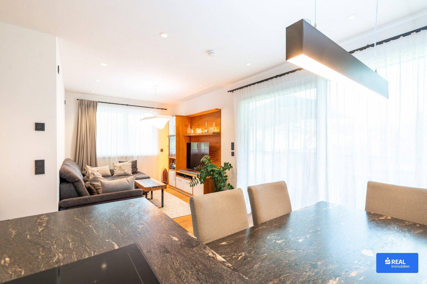 Heller offener Wohn-Essbereich mit großzügigen Fenstern und modernem Sofa.