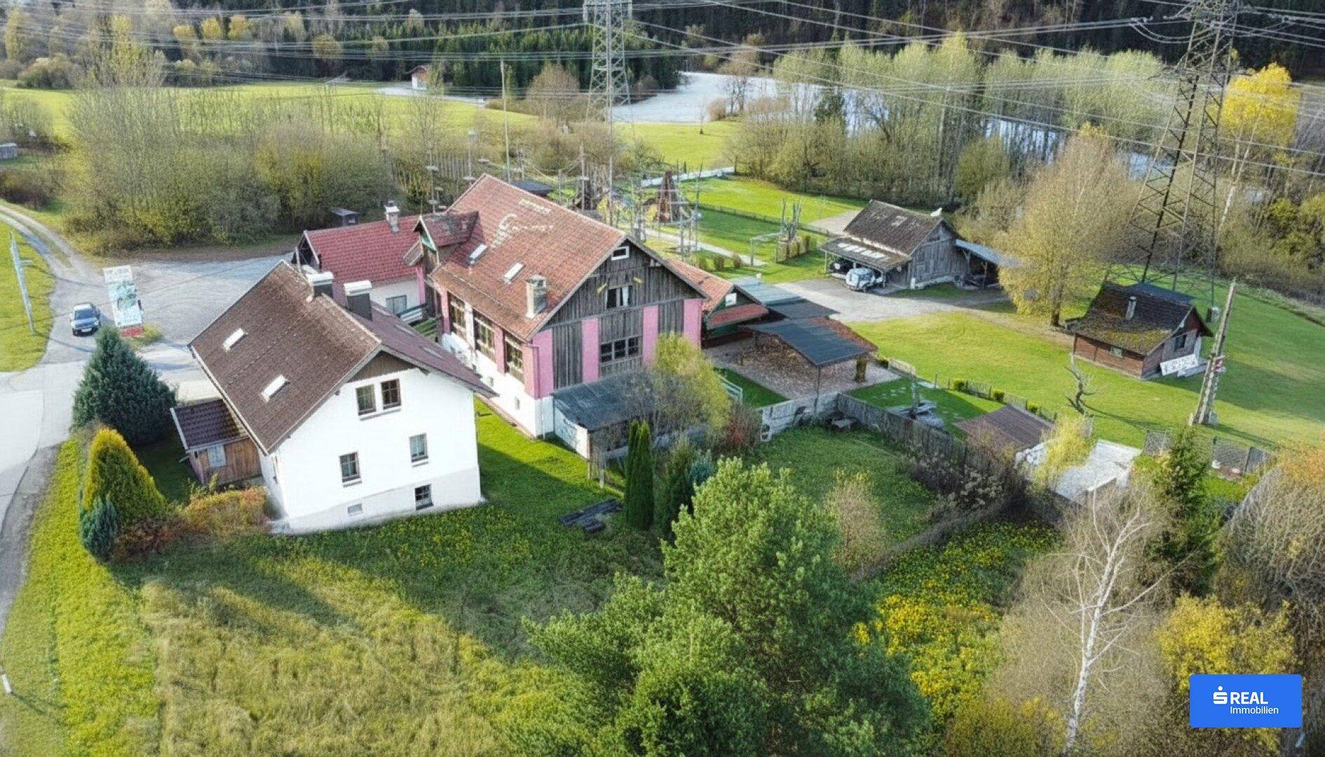 Luftaufnahme des Anwesens mit mehreren Gebäuden, umgeben von grüner Landschaft und Bergen.