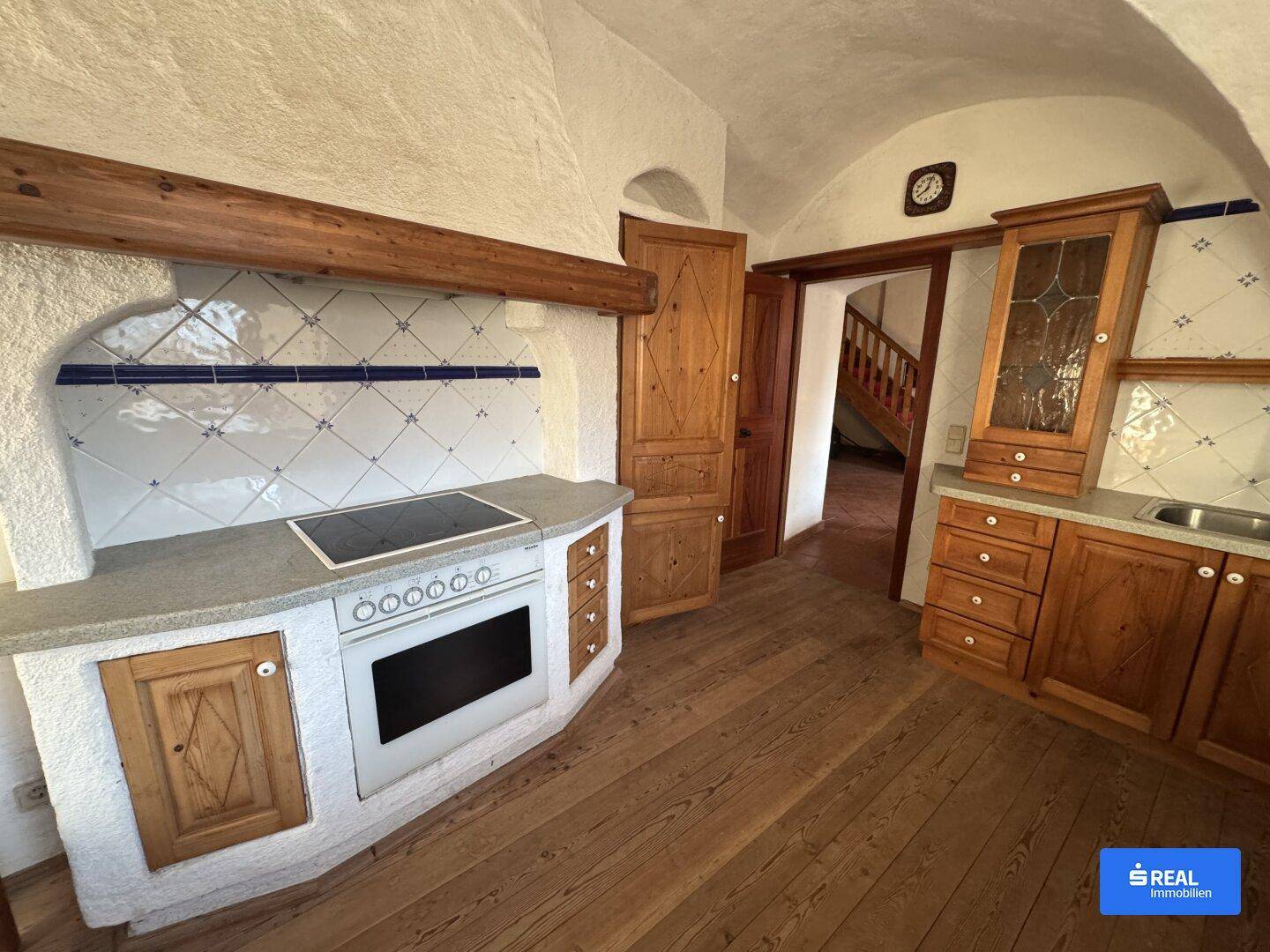 Traditionelle Küche mit Holzdielenboden, gemauertem Herd und blauen Fliesenakzenten.