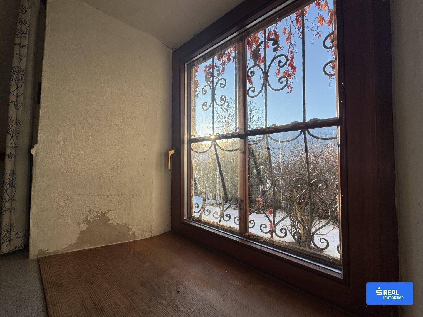 Fenster mit schmiedeeisernem Gitter und Blick auf eine verschneite Winterlandschaft.