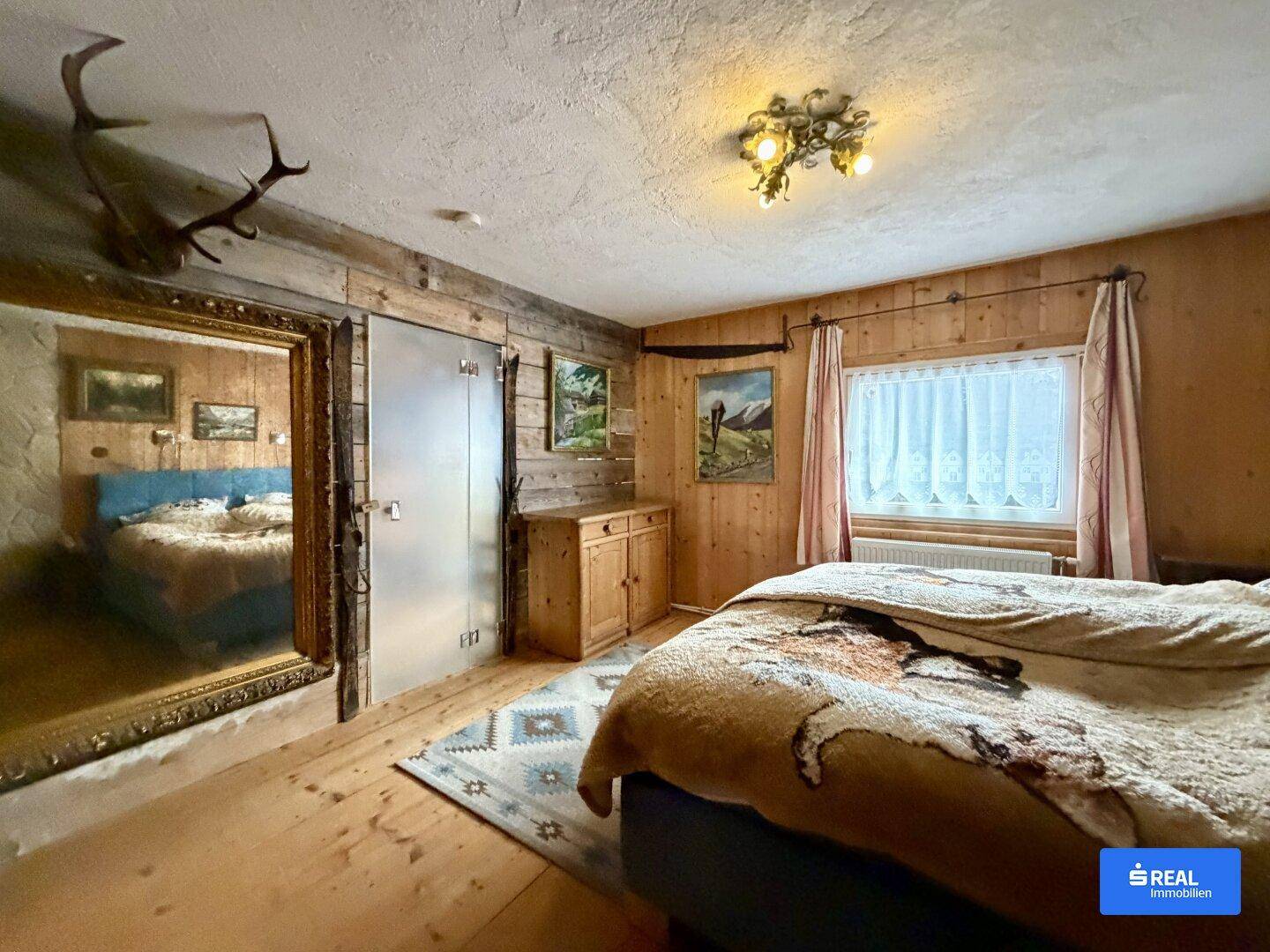 Schlafzimmer im alpinen Stil mit Holzwänden, großem Spiegel und gemütlichem Bett.