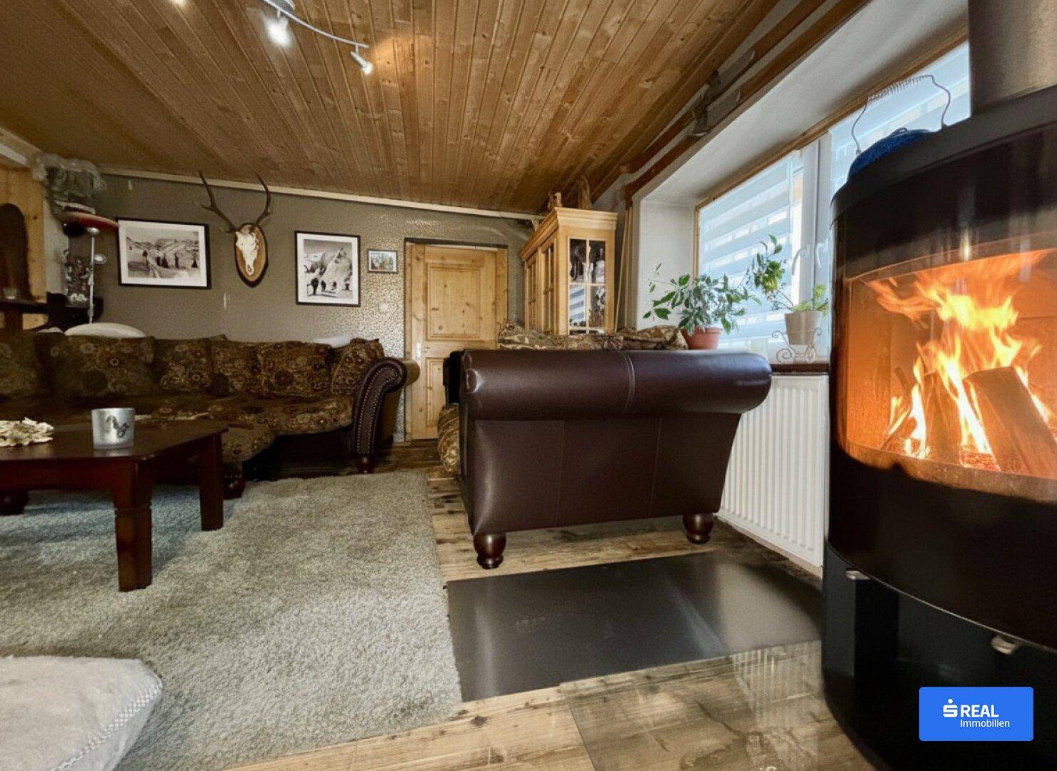 Rustikales Wohnzimmer mit Holzbalkendecke, Kaminofen und gemütlicher Sitzecke.