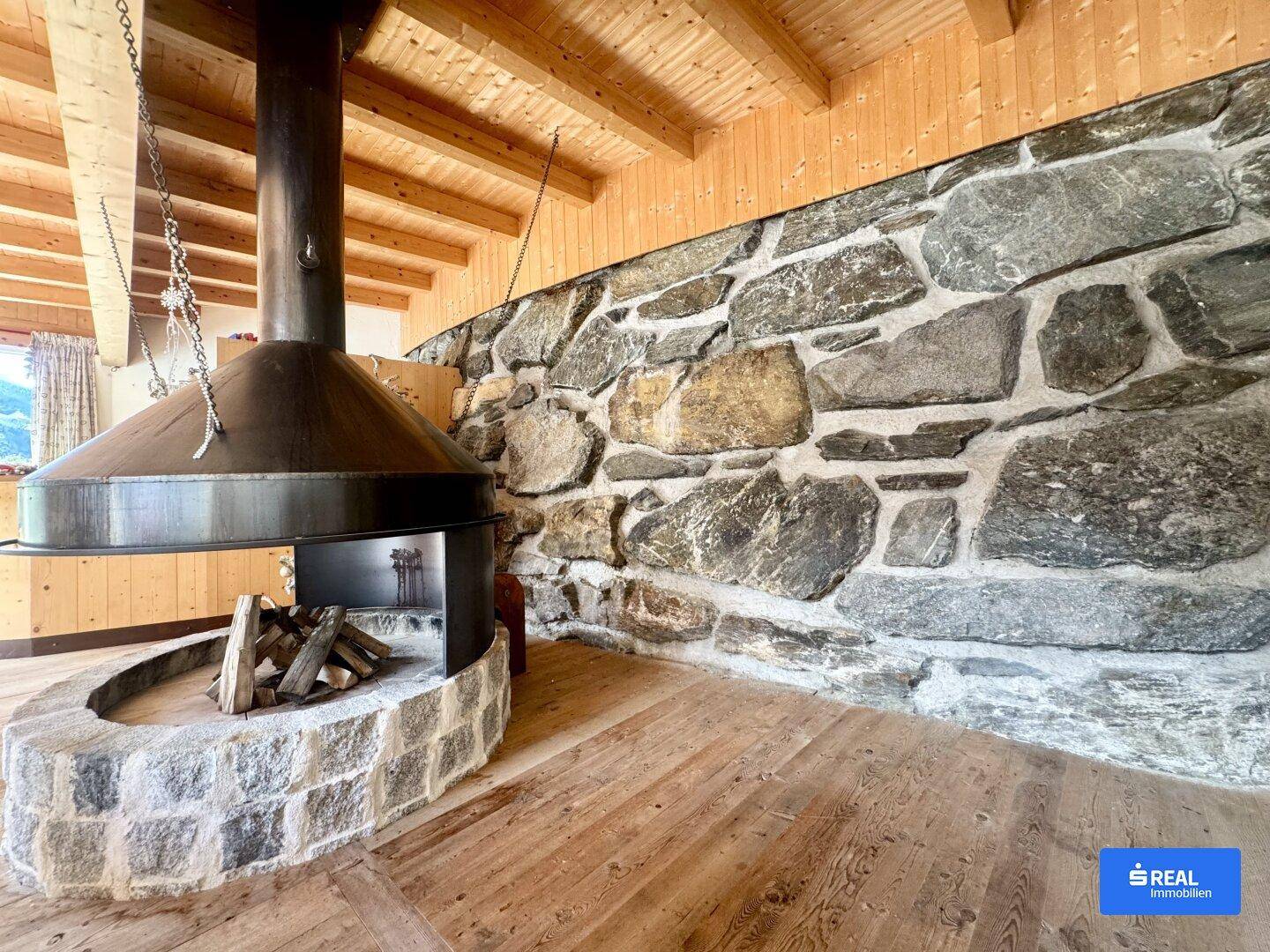 Geräumiges Wohnzimmer mit rustikaler Steinwand, Holzboden und einem markanten Kamin.