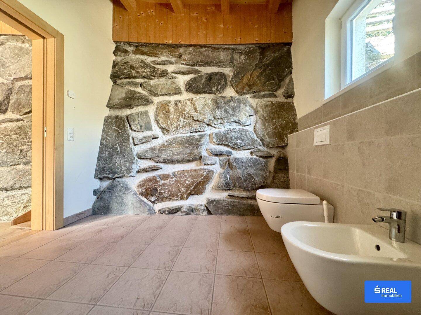 Modernes Badezimmer mit Fliesenboden, rustikaler Steinwand und separatem Bidet.