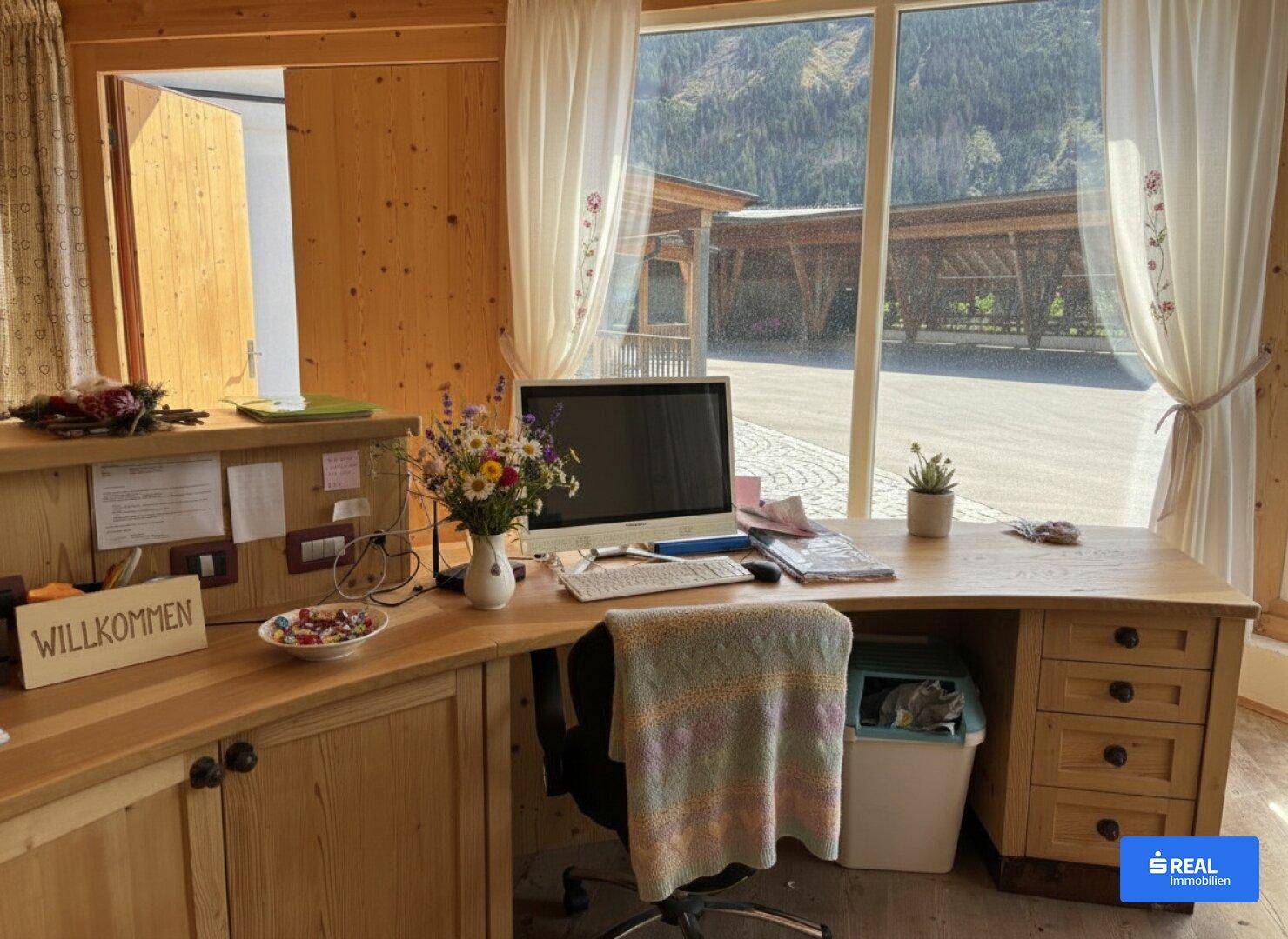 Gemütlicher Empfangsbereich oder Büro mit Holzmöbeln und Blick auf die Außenanlage.