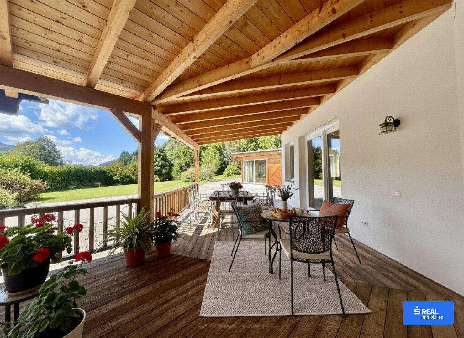Geräumige Holzterrasse mit Esstischen und Blick auf die umliegende Natur und Berge.