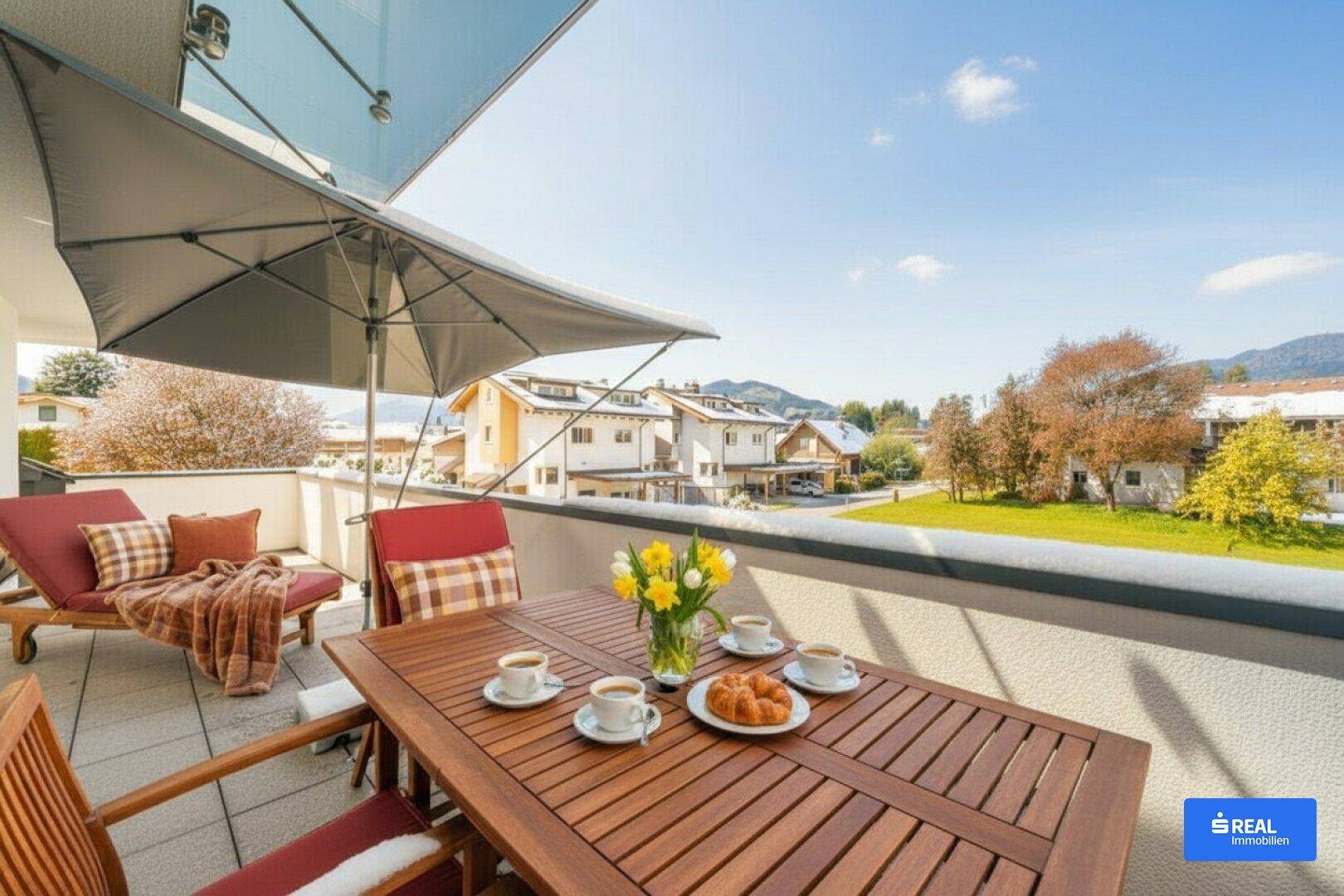 Möblierter Balkon mit Esstisch, Liegestuhl und weitem Blick auf die umliegende Landschaft und Berge.