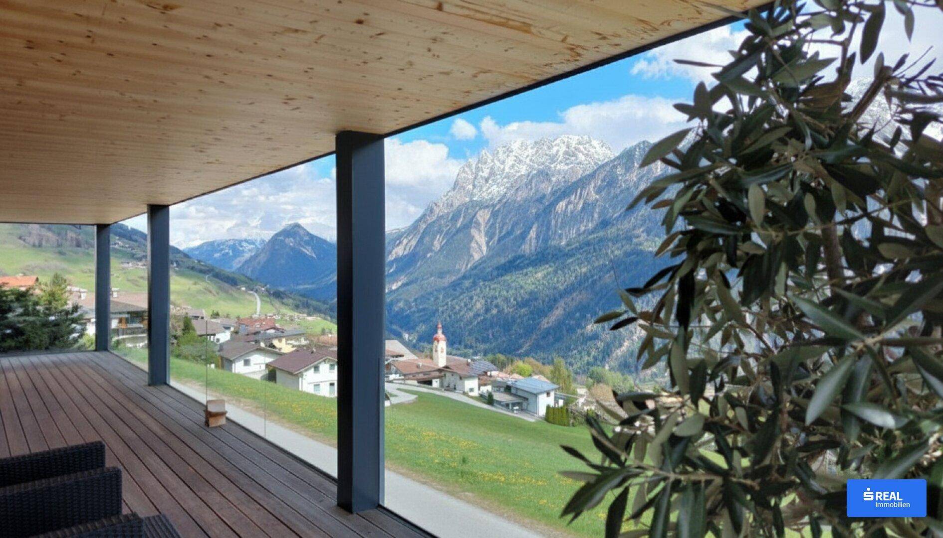 Geräumige überdachte Terrasse mit Holzboden und atemberaubendem Panoramablick auf die umliegende Bergwelt.
