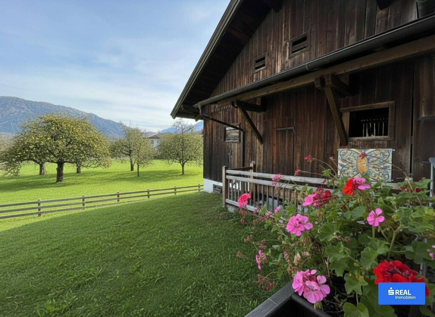 Rustikaler Balkon mit bunten Blumen und weitem Blick auf den grünen Garten und die Berge.