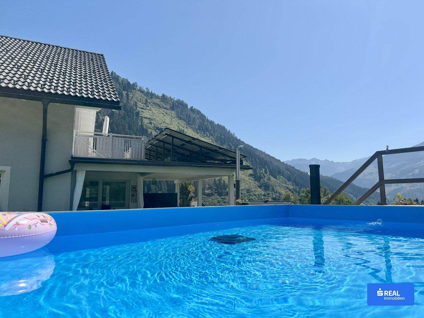 Blauer Aufstellpool im Garten mit Blick auf das Haus und die umliegende Berglandschaft.