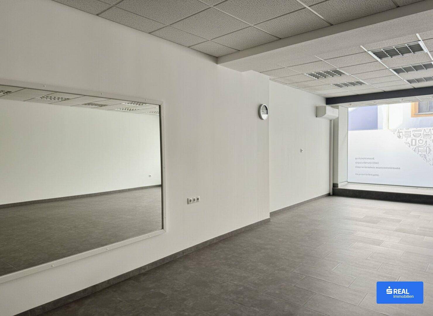 Heller Gewerberaum mit großem Wandspiegel, Fliesenboden und abgehängter Decke.