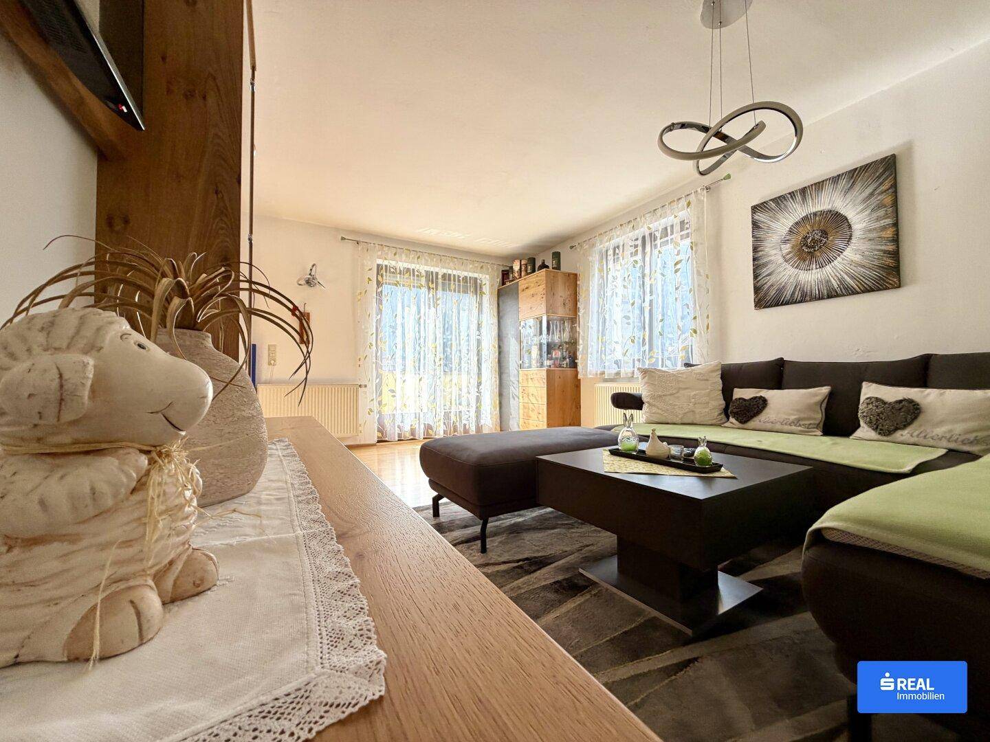 Gemütliches Wohnzimmer mit großem Sofa, Holzboden und Zugang zu einem Balkon oder einer Terrasse.