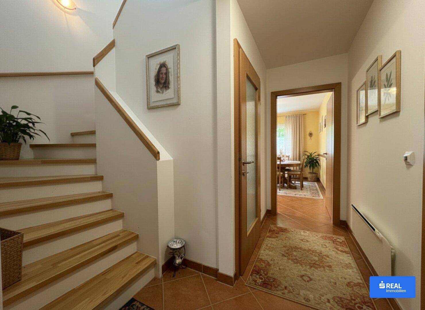 Heller Flur mit Holztreppe, Terrakottaboden und Zugang zu weiteren Räumen.