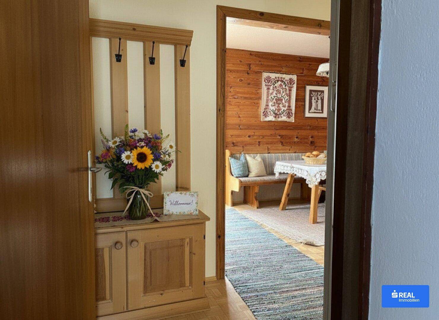 Heller Eingangsbereich mit Garderobe, Blumenstrauß und Blick in den traditionellen Essbereich.