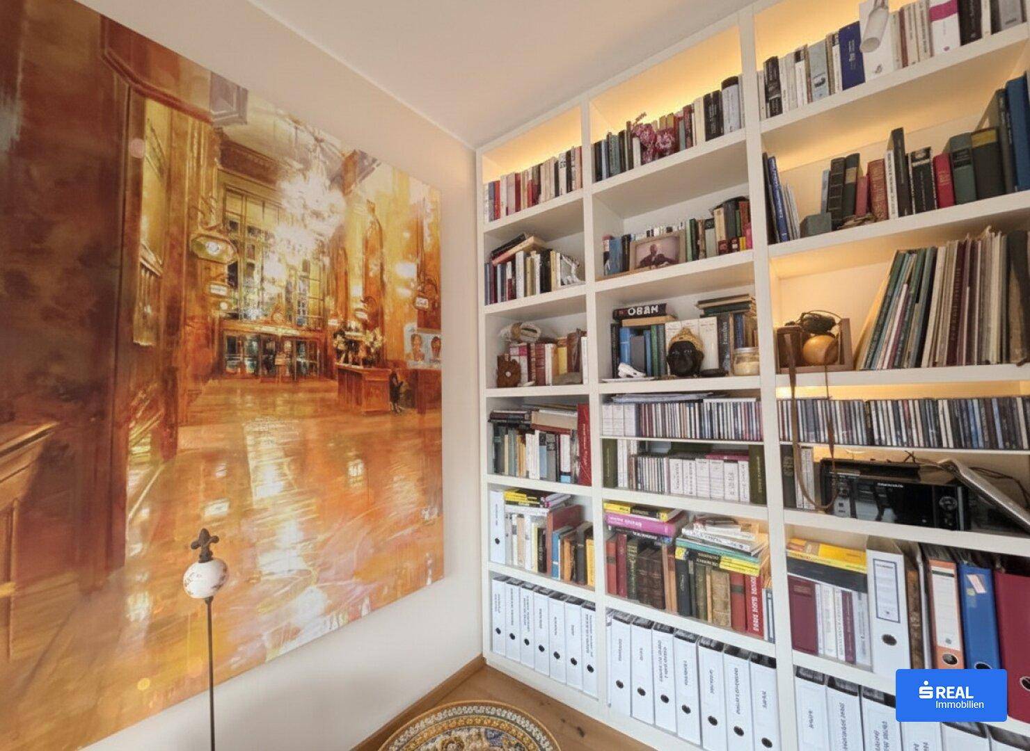 Gemütlicher Bibliotheksbereich mit beleuchteten Einbauregalen und einem großen Kunstwerk an der Wand.