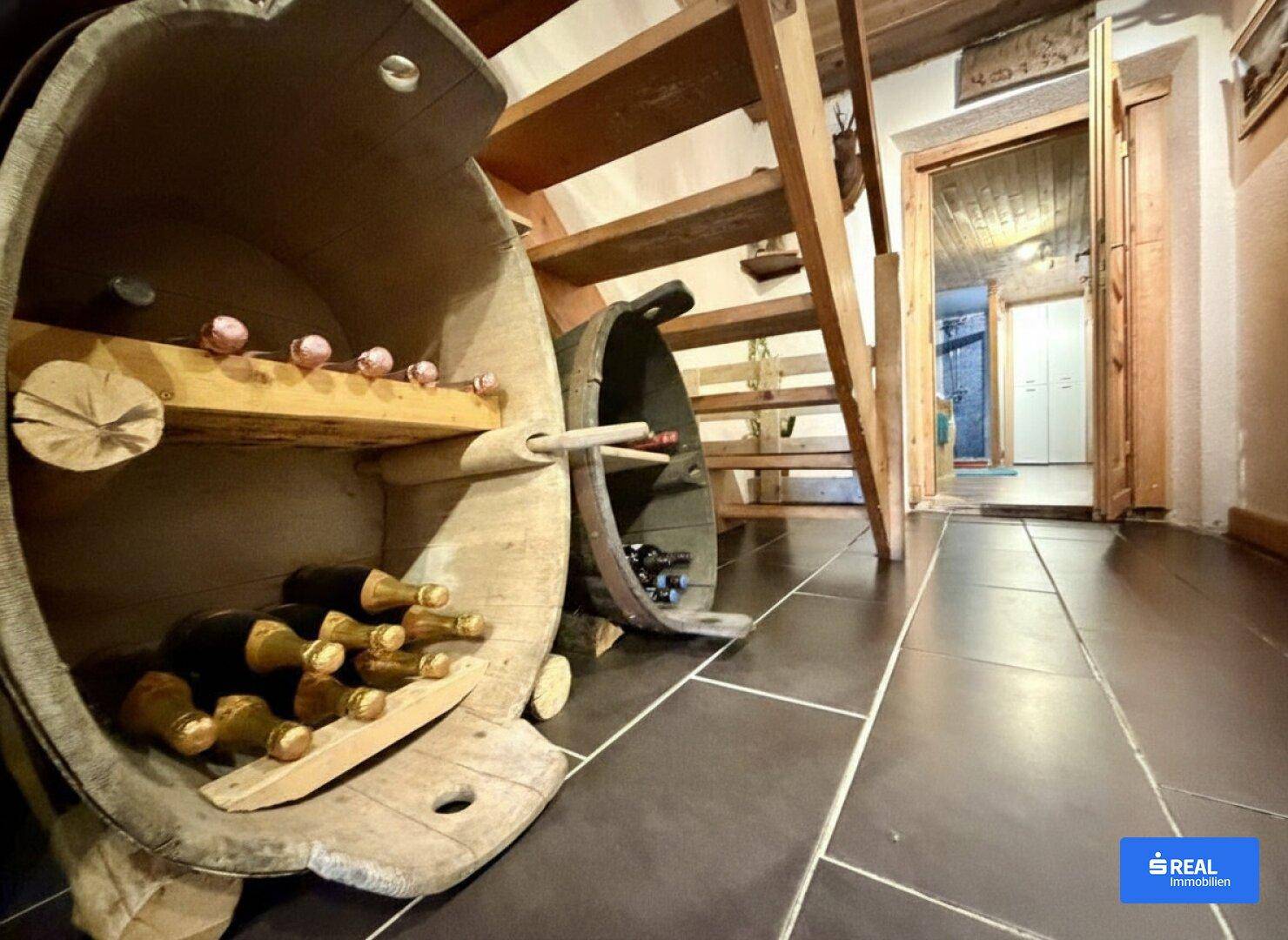 Flur mit dunklen Fliesen, Holztreppe und kreativer Weinlagerung in Holzfässern.