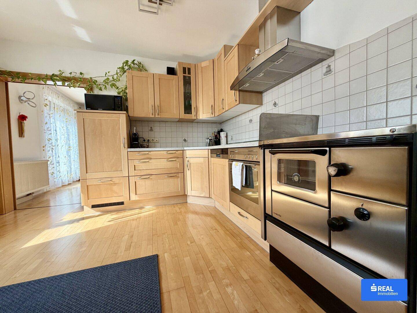 Funktionale Küche mit Holzschränken, Fliesenrückwand und einem traditionellen Holzofen mit Backfach.