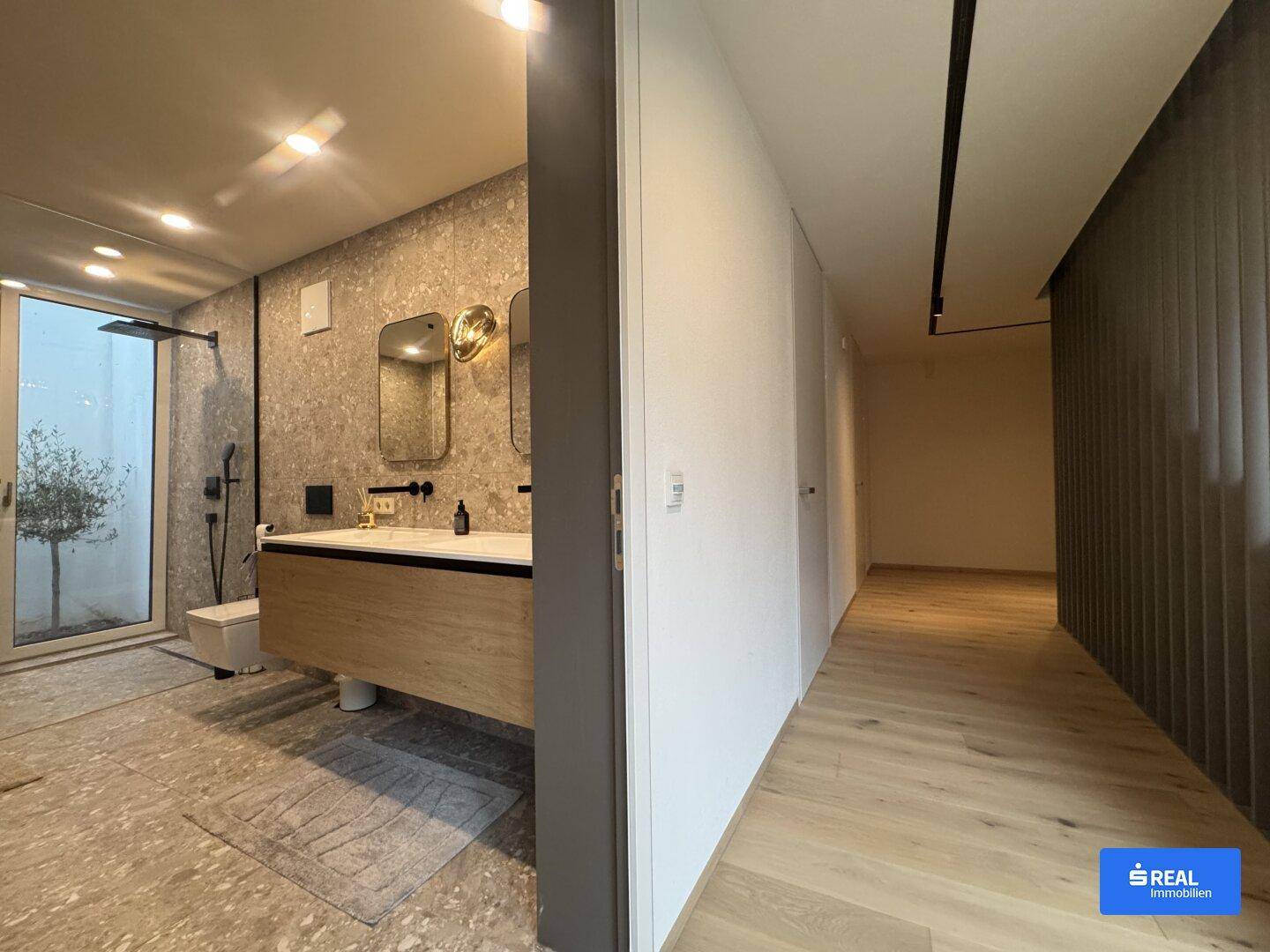 Modernes Badezimmer mit begehbarer Dusche, großem Fenster und angrenzendem Flur mit Holzboden.