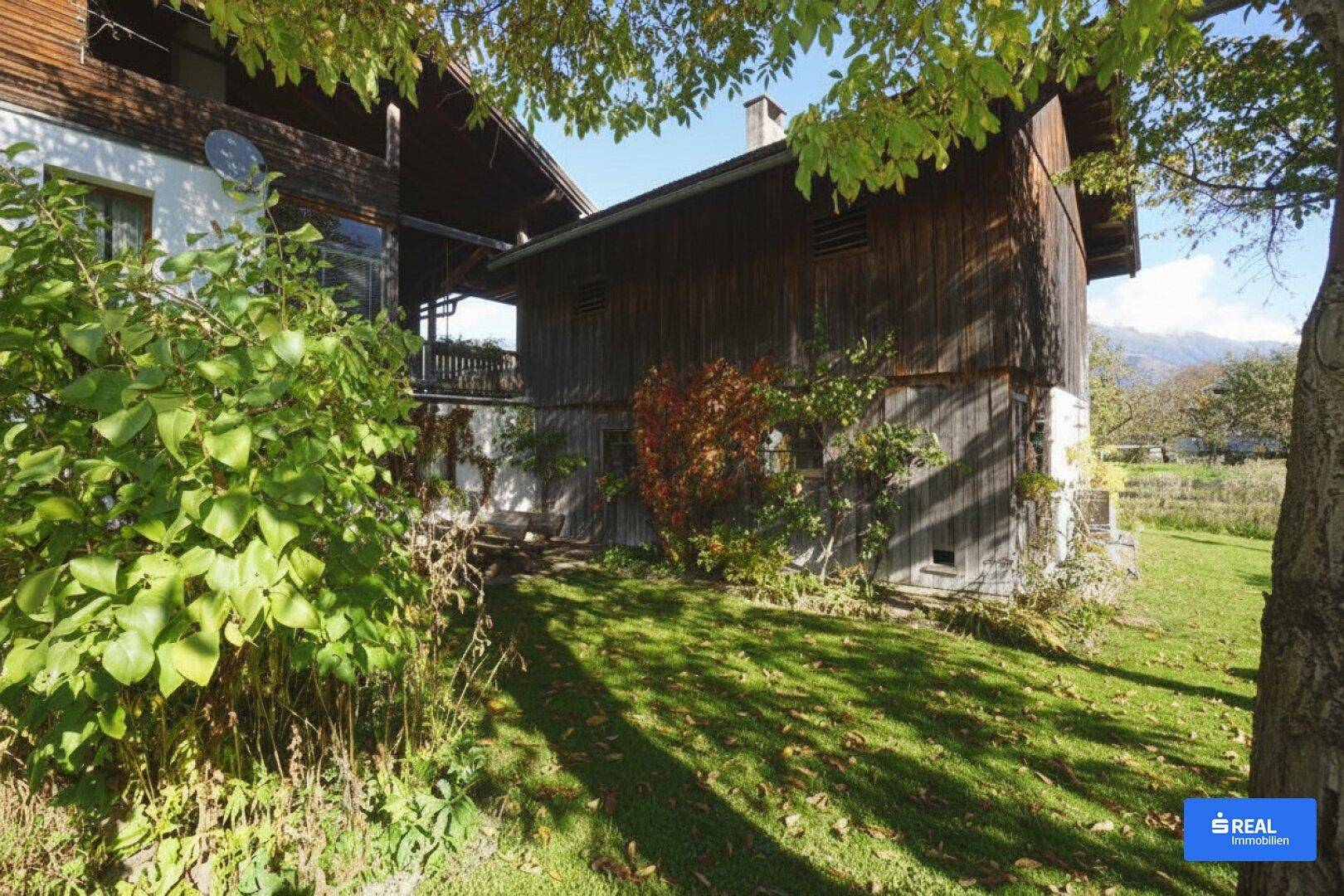 Blick auf das rustikale Holzhaus mit gepflegtem Garten und herbstlicher Bepflanzung unter blauem Himmel.