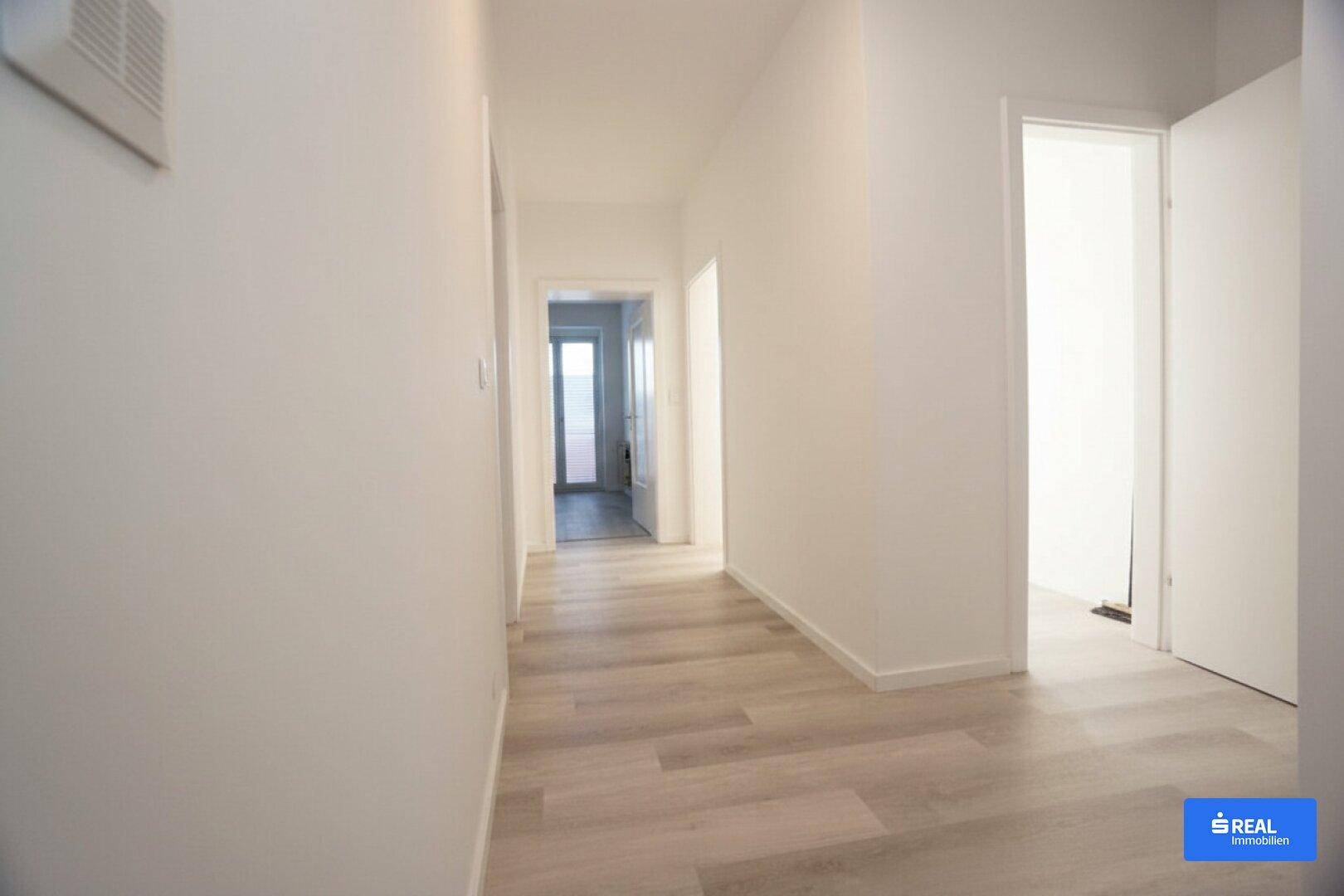 Langer, heller Flur mit Laminatboden und Zugang zu mehreren Zimmern, in neuwertigem Zustand.