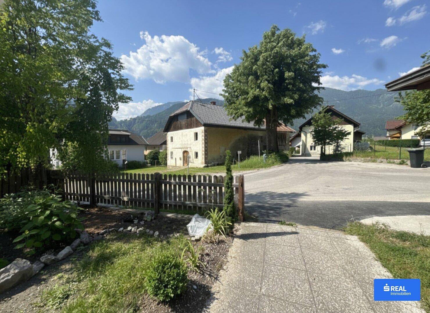 Blick auf die ländliche Umgebung mit weiteren Häusern und einer Berglandschaft im Hintergrund.