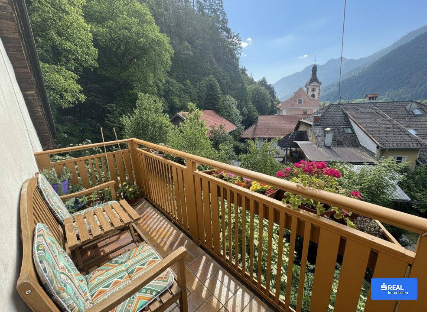 Gemütlicher Balkon mit Holzbalkonmöbeln und weitem Blick über das Dorf und die umliegenden Berge.