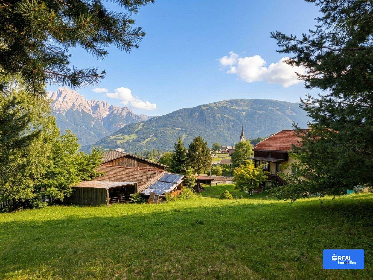 Malerische Aussicht auf ein Dorf und die Alpen von einem sonnigen Grundstück mit Grünflächen.