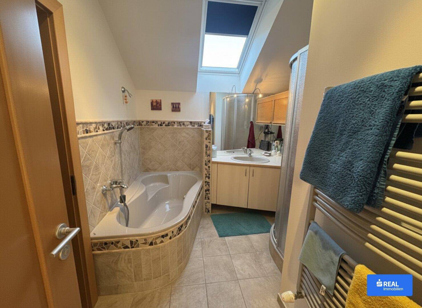 Badezimmer mit Eckbadewanne, Dusche, Waschtisch und einem Dachfenster für natürliches Licht.